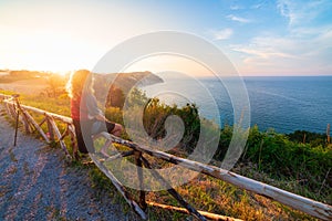 Woman rear view watching sunset landscape Conero natural park dramatic coast headland rocky cliff adriatic sea beautiful sky