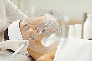 Woman receiving apparatus facial microcurrent treatment from therapist in beauty salon