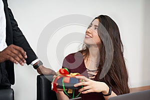 Woman receiving a beautiful gift from her male colleague while working in the office, relationships concept