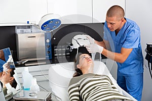 Woman receiving facial light therapy in aesthetic medicine office