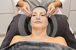 Woman receiving facial skin treatment from crop masseuse in beauty center