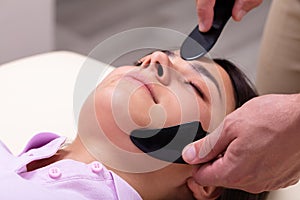 Woman Receiving Gua Sha Acupuncture Treatment On Her Face