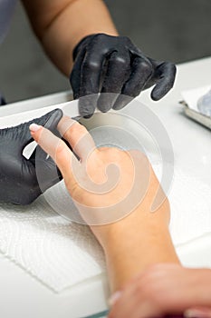 Woman receiving a manicure with nail file by a manicure master in a nail salon.