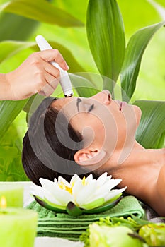 Woman receiving microdermabrasion therapy against leaves