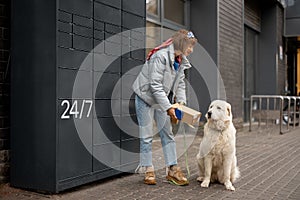 Woman receiving a parcel from automatic post machine during a walk with her dog