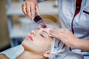 Woman receiving ultrasonic facial exfoliation at cosmetology salon.