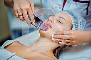 Woman receiving ultrasonic facial exfoliation at cosmetology salon.