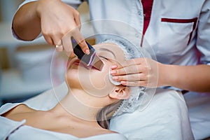 Woman receiving ultrasonic facial exfoliation at cosmetology salon.