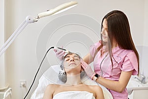 Woman receiving ultrasonic facial exfoliation at cosmetology salon. Procedure clearing clogged pores, ultrasonic treatment for