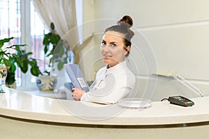 Woman receptionist in medical coat stands at reception desk