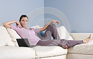 Woman reclining on couch at home with laptop