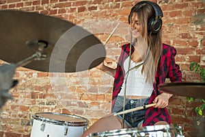 Woman recording music, singing and playing drums while sitting in loft workplace or at home