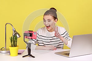 Woman recording video for followers, looking at phone camera, talking with followers, showing v sign