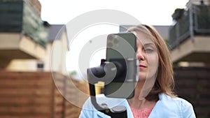 A woman is recording video using a smartphone with a stabiliser. Social media and video blogging, outdoor portrait woman