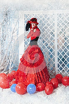 Woman in a red antique dress is freezing under the falling snow.