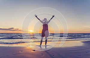 Woman in red with arms outstretched by the sea at sunrise enjoying freedom and outdoors life