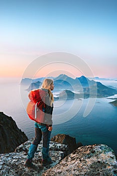 Woman with red backpack hiking in Norway girl traveler on mountain cliff edge in Lofoten islands