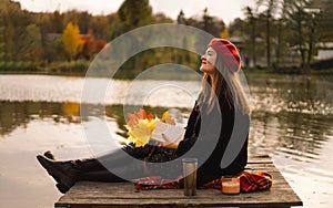 Woman in a red beret reading book on wooden pontoon. Autumn season.