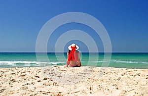 Woman in red bikini and hat sitting in peace on a beautiful sunny beach.