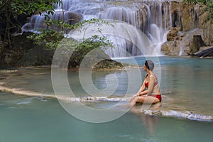 Woman in red bikini look water at Erawan Waterfall and natural