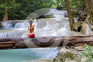 Woman with red bikini sit on timber at Erawan Waterfall and natural