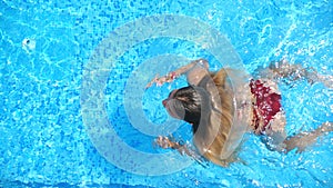 Woman in red bikini swimming through pool with crystal clear water. Elegant lady relaxing on tropical resort during