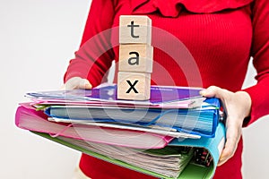 A woman in a red blouse is holding a stack of document folders and pads with the words Tax, Taxes and billing, paperwork concept