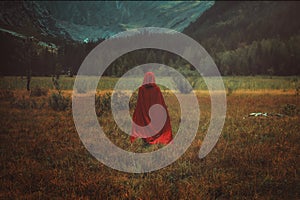 Woman with red cloak in a mountain valley