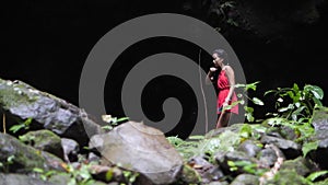 Woman in red clothes walking alone in a wet narrow dark gorge at the jungle.