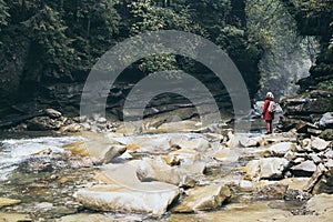 Woman in red coat standing on the banks of deep mountain river in Yaremche, Ukraine