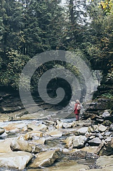 Woman in red coat standing on the banks of deep mountain river in Yaremche, Ukraine