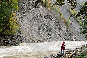 Woman in red coat standing on the banks of deep Prut river in Yaremche, Ukraine