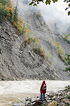 Woman in red coat standing on the banks of deep Prut river in Yaremche, Ukraine