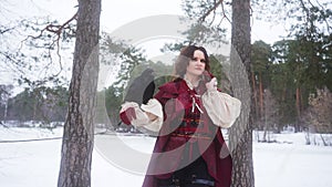 a woman in a red coat is standing next to a tree in the snow