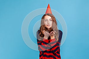 Woman in red cone sending air kisses, celebrating her birthday, expressing love to her guests.