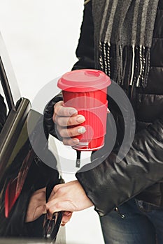 Woman with a red cup of hot drink keeps the car door handle