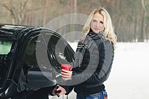 Woman with a red cup of hot drink keeps the car door handle