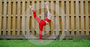 Woman in red does stretching and yoga exercices for legs in the yard of an apartment building, fitness in the urban