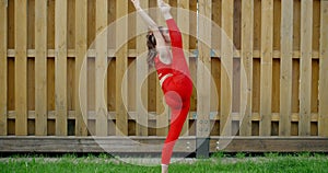 Woman in red does stretching and yoga exercices for legs in the yard of an apartment building, fitness in the urban