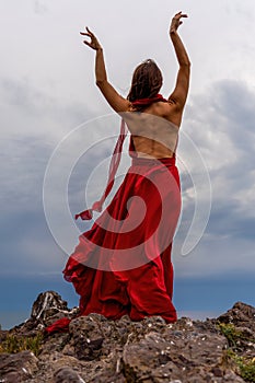 Woman in red dress dance over storm sky, gown fluttering fabric flying as splash