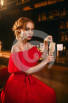 Woman in red dress drinks cocktail at bar counter