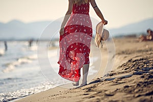 Woman in red dress enjoying at walking on the beach at sunset