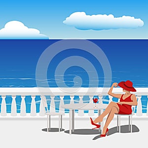 woman in a red dress and hat sits on a chair in a summer cafe on the embankment near the sea