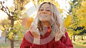 Woman in red dress hides face with yellow leaves in park