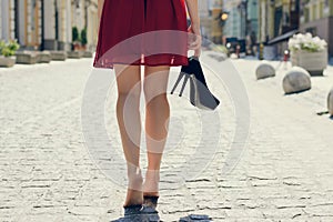 Woman in red dress, with high heel shoes in hand, walking in the