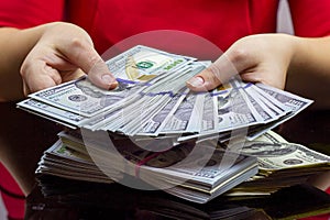 Woman in red dress holdind and counting cash money american dollars in her hands on black table background