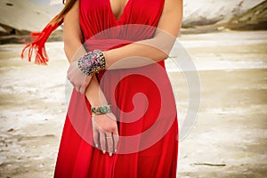 A woman in a red dress holds her hands in front. The woman is wearing beautiful bracelets.