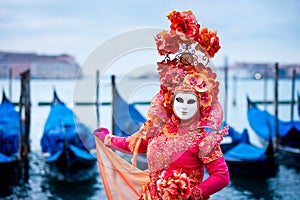 Woman in red dress masked for Venice Carnival in front of typical gondola boats