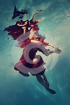 A woman in a red dress poses underwater as if she is flying