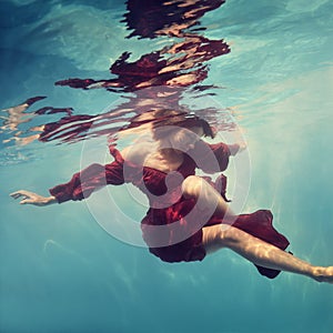 A woman in a red dress poses underwater as if she is flying